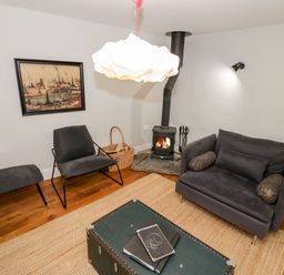 A small living room with a black chair and ottoman a two-seater sofa a wood-burning stove and a trunk used as a coffee table at The Old Stables in Chipping Campden
