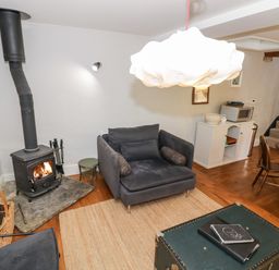 A living room with a wood burning stove armchairs a rug a chest and a dining table at The Old Stables in Chipping Campden