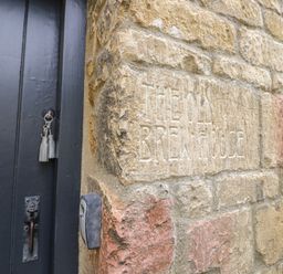 A stone wall with the words The Old Brewhouse carved into it next to a black door with keys in the lock at The Old Brewhouse in Chipping Campden