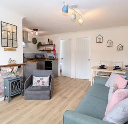 A living room with a sofa and armchair next to a small stove and a dining table with two place settings at 72 in Hemsby