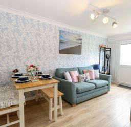 A living room with a dining table set for four and a sofa with cushions at 72 in Hemsby