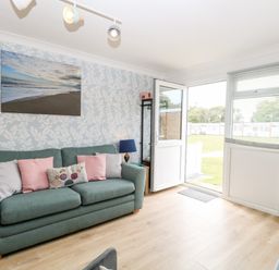 A living room with a green sofa and cushions next to an open door and large window at 72 in Hemsby