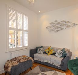 A living room with a grey sofa covered by a throw with cushions a green armchair a grey padded bench with a fur throw and metal fish wall decor at The Cottage in Weymouth