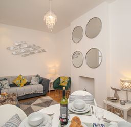 A living room with a sofa, green armchair, round mirrors, dining table with dishes and wine bottle at The Cottage in Weymouth