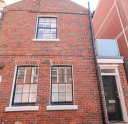 Exterior view of a brick building with three windows and a black door at The Cottage in Weymouth