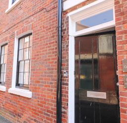 A black front door with two signs next to it on a brick building with two windows at The Cottage in Weymouth