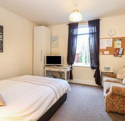 A bedroom with a bed sofa television on a white table and a window with dark curtains at The Studio in Sheringham