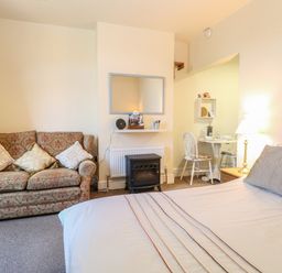 A room with a bed a patterned sofa a small dining table and a stove at The Studio in Sheringham