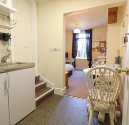 A kitchenette with a sink and cabinets next to a small dining table and chairs leading into a bedroom with a window and a bed at The Studio in Sheringham