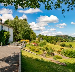 A house with an outdoor dining table and chairs next to a garden and fields at Fron Dderw in Bala