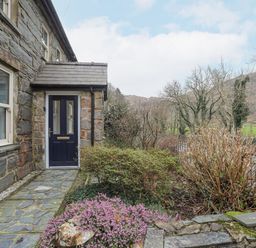 An entrance door to a stone house with a stone path and garden with bushes and flowers at Glyn Awel in Nant Gwynant near Beddgelert