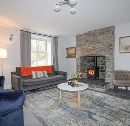 A living room with a stone fireplace a round white coffee table and sofas at Glyn Awel in Nant Gwynant near Beddgelert
