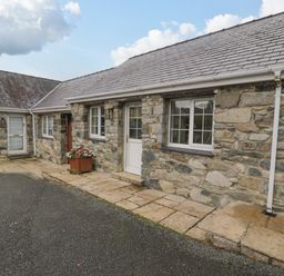 Exterior view of a stone house with two windows, two doors, a flower planter, and a paved walkway at Bwythyn Yr Wyddfa in Llanberis