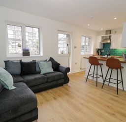 A living room with a sectional sofa and a kitchen with stools and teal tile backsplash at Bwythyn Yr Wyddfa in Llanberis