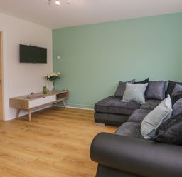 A living room with a grey sectional sofa and a wooden media console with a wall-mounted TV at Bwythyn Yr Wyddfa in Llanberis