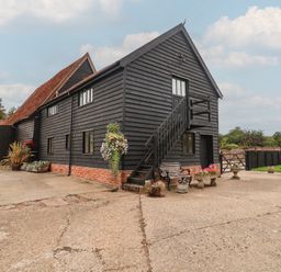 An outdoor view of a black barn with steps and flower pots at The Cow Shed in Chediston near Halesworth