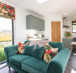 A kitchen and living area with a green sofa pillows and floral blinds at Brow Wood Cabin in Ullswater