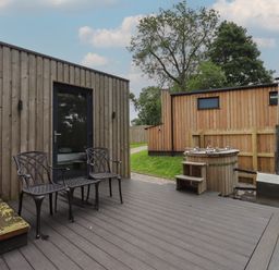 An outdoor patio with two black chairs a wooden hot tub and a wooden cabin in the background at Brow Wood Cabin Ullswater