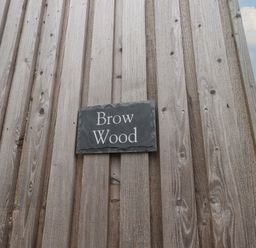 A wooden wall with a black sign that reads Brow Wood at Brow Wood Cabin in Ullswater