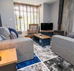 A living room with gray sofas a striped armchair coffee table tv and wood stove at The Dollhouse in Cayton Bay