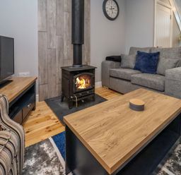 A living room with a wood-burning stove a grey sofa blue cushion a striped armchair wooden coffee table and a television at The Dollhouse in Cayton Bay