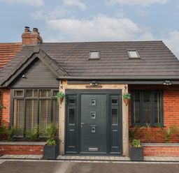 The front exterior of a brick house with a dark door two windows and plants at The Dollhouse in Cayton Bay