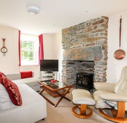 A living room with a stone fireplace a beige recliner a grey sofa and a wooden coffee table at Ty Nain in Beddgelert