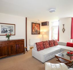 A living room with a gray sofa and red cushions a wooden sideboard with flowers and two paintings at Ty Nain in Beddgelert