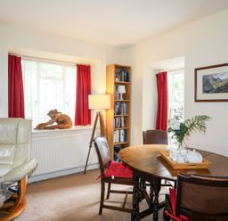 A dining room with a round wooden table and chairs with red cushions and a cream armchair at Ty Nain in Beddgelert