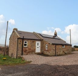 A stone cottage with solar panels on the roof near a country road at Henhill Lodge in Chathill near Seahouses