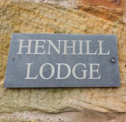 A black plaque with white text reading Henhill Lodge attached to a stone wall at Henhill Lodge in Chathill near Seahouses