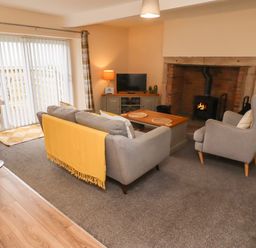 A living room with grey sofa and armchair a wooden coffee table a fireplace and a TV at Henhill Lodge in Chathill near Seahouses