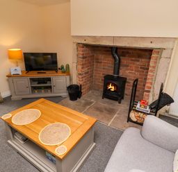 A living room with a wood stove in a brick fireplace and a TV on a cabinet at Henhill Lodge in Chathill near Seahouses
