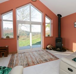 A living room with a stove and large windows at Y Stabal near Llanilar