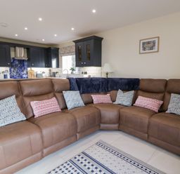 A living room with a brown sofa and kitchen cabinets at Beudy near Llanilar