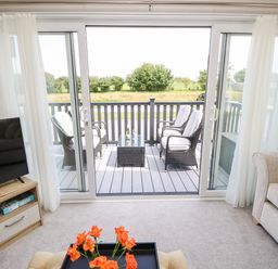 A living area with a sofa orange flowers on a table a television and a balcony with chairs at 7 Wild Haven in Landford