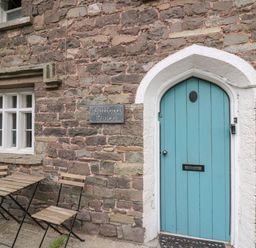 A stone wall with a blue arched door and wooden chairs and table outside at Clifford Place