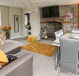 A living room with a sofa pillows a dining table chairs a wall clock and a television above a stone fireplace at Yewtree Cottage in Defynog near Sennybridge
