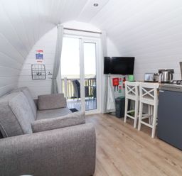 A compact living area with a gray sofa TV kitchen appliances and two bar stools at Owl's Nook Kilkhampton