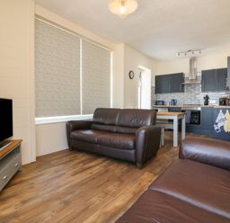 A living room with two brown leather sofas a television and an open kitchen with blue cabinets at At the Bay Apartment in Hele Bay Ilfracombe