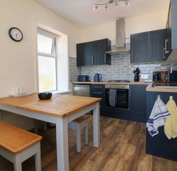 A kitchen with wooden table and benches navy cabinets stove and microwave at At the Bay Apartment in Hele Bay Ilfracombe
