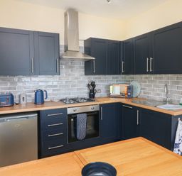 A kitchen with dark blue cabinets a stainless steel oven and fridge a wooden countertop and grey tiled backsplash at At the Bay Apartment in Hele Bay Ilfracombe