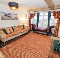 A sitting room with beige sofas orange cushions a purple chaise longue orange rug and window with curtains at Riverside Manor in Evesham
