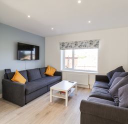 A living room with two gray sofas, a white coffee table, a wall-mounted TV, and a window with a patterned blind at Whitby View in Whitby