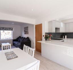 A kitchen with white cabinets and an island next to a dining area with a table and chairs and a living room with a sofa and a window at Whitby View in Whitby