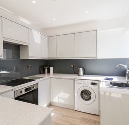 A kitchen with white cabinets a washing machine an oven stovetop a kettle and a sink at Whitby View in Whitby