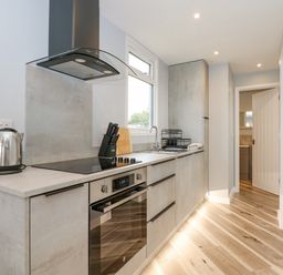 A narrow kitchen with a countertop electric stove oven sink and cabinets at Number 9 in California Norfolk