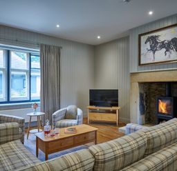 A living room with plaid sofas and armchairs a coffee table and a fireplace with a horse painting above at The Filly in Humshaugh