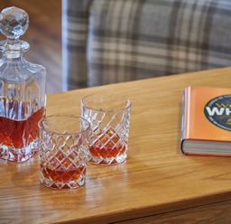 A wooden table with a glass decanter and two glasses containing whisky and a book about whisky on the side at The Filly in Humshaugh