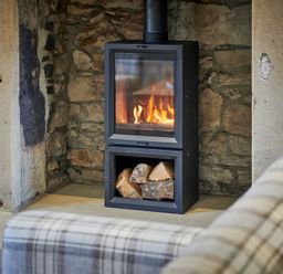 A wood burning stove with fire and logs inside a stone fireplace at The Filly in Humshaugh